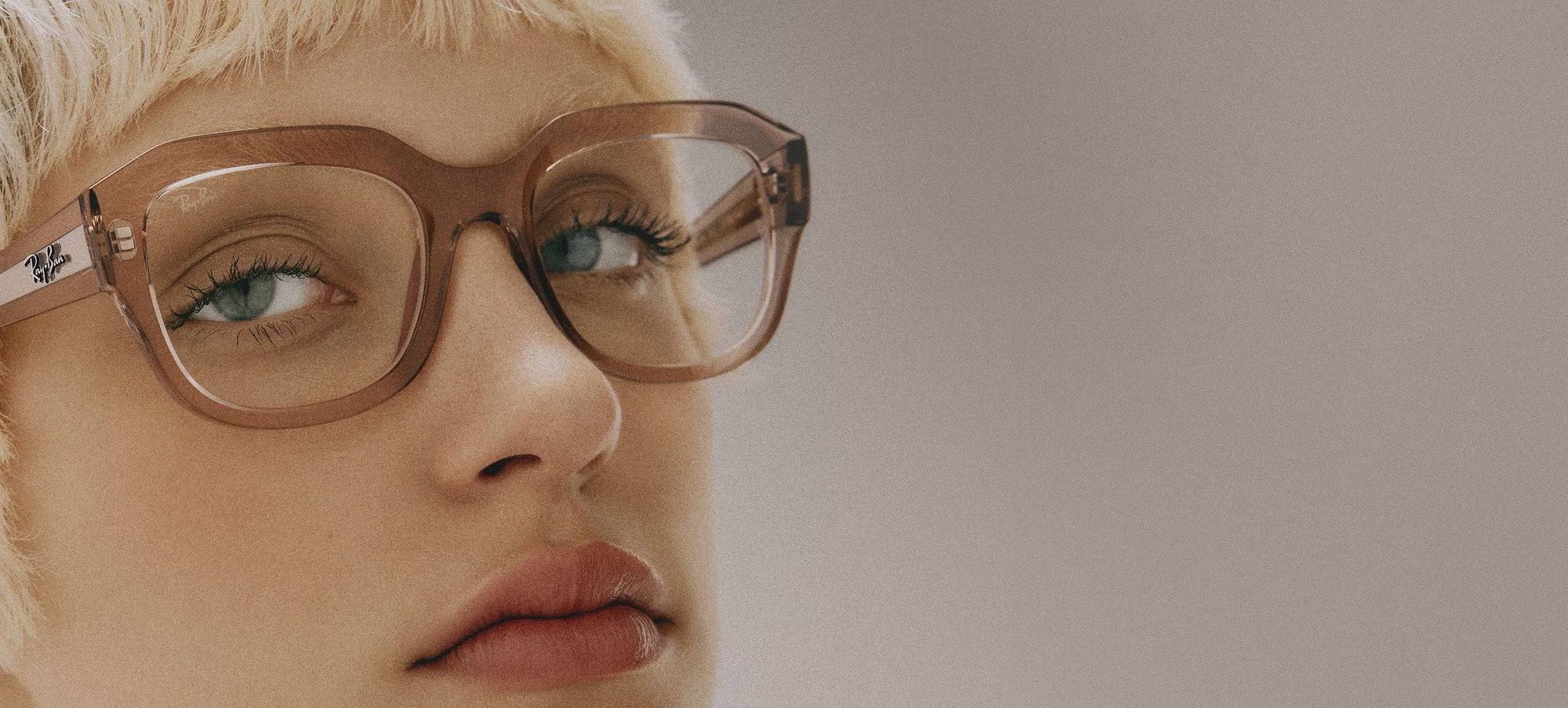 Kısa sarı saçlı bir model, şeffaf pudra tonlu kalın asetat Ray-Ban numaralı gözlükle yakın plan portrede
